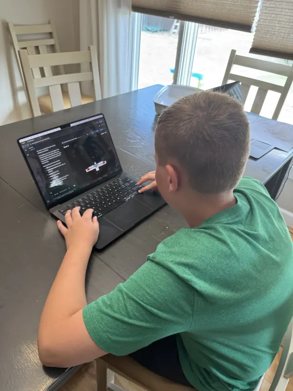 Over-the-shoulder view of a child using a laptop with a game and AI chat on screen.